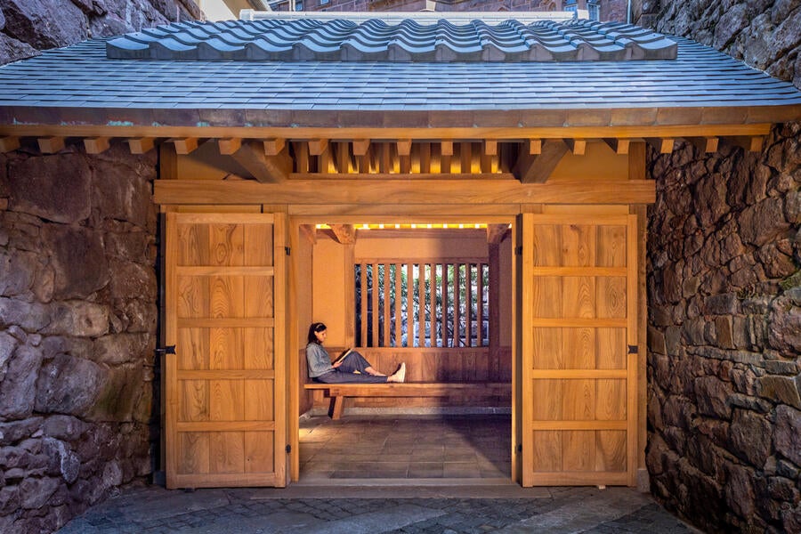 Person sitting on a bench inside of a Japanese Tea Gate, reading a book.